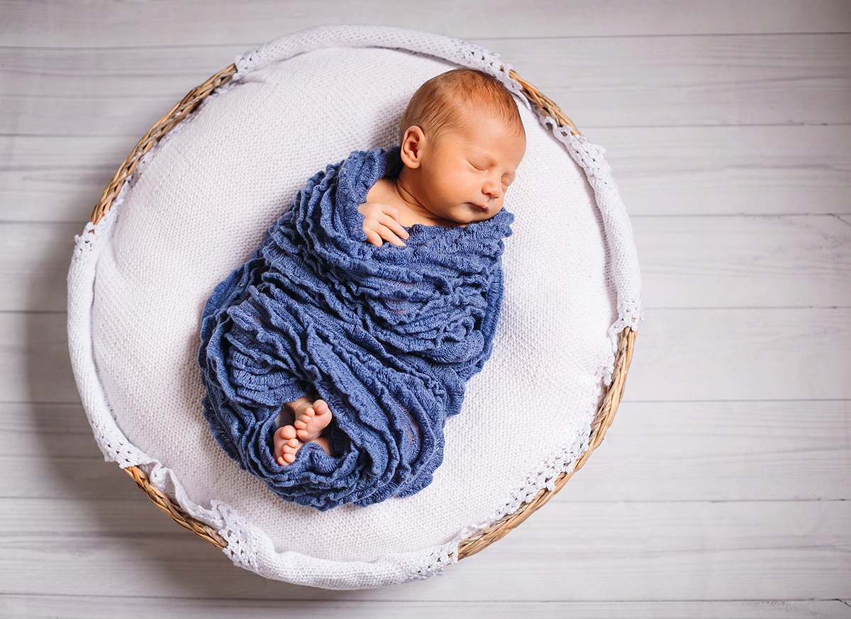 newborn-baby-enveloped-blue-scarf-sleeps-white-pillow copy